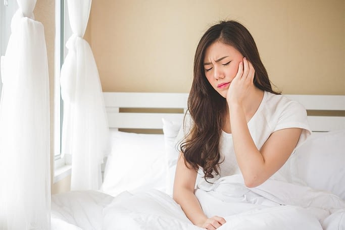 Women holding site of jaw and face because of eagle syndrome pain while sitting in bed