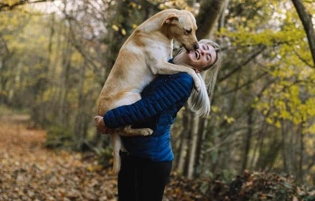 woman with dog in woods laughing and hugging