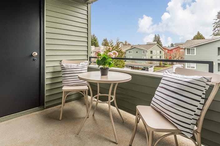 Two chairs with striped pillows, and a small table with a potted plant sit on the balcony at a Haller Post Apartment